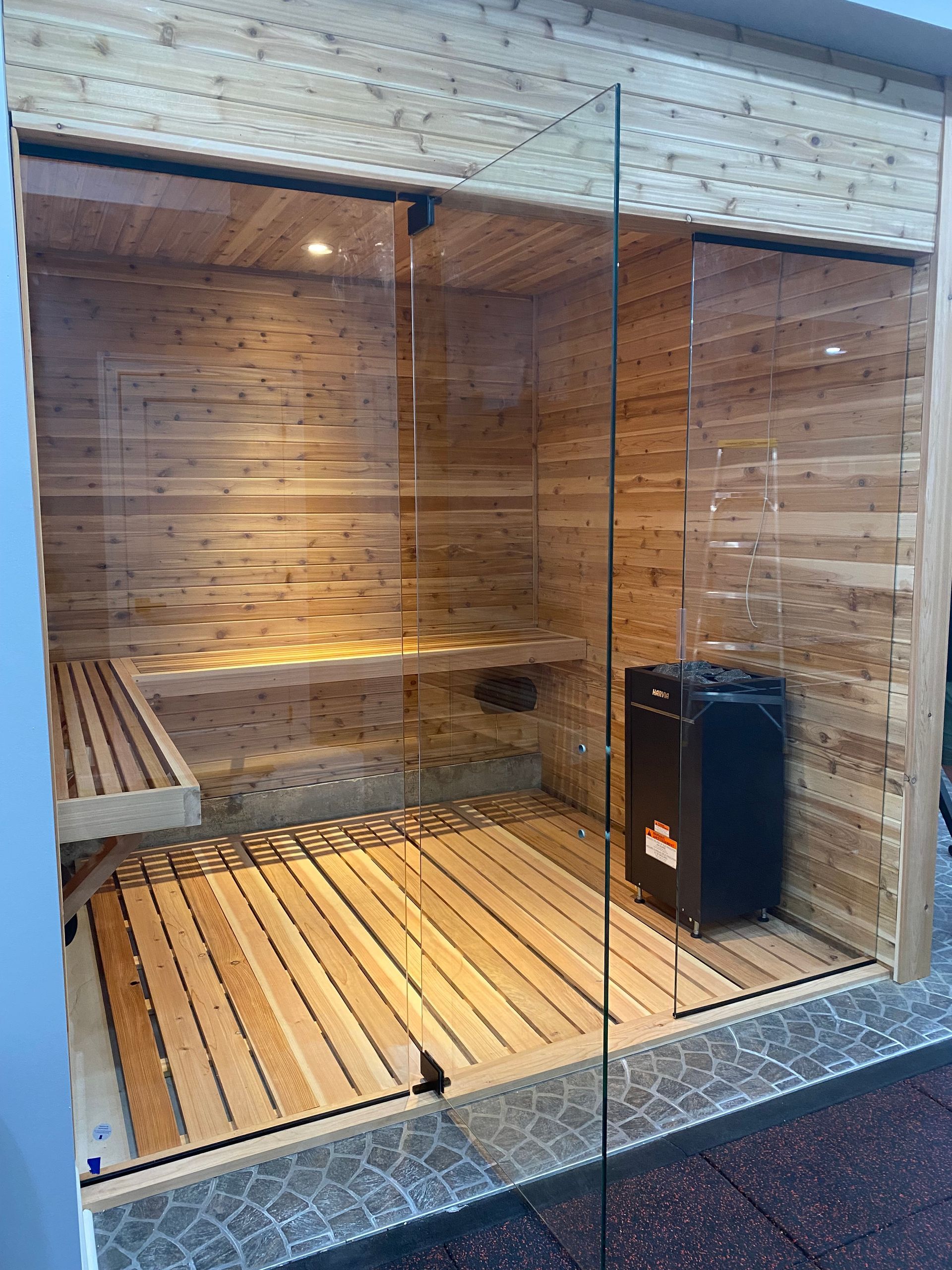 Modern wooden sauna interior with glass wall, bench seating, and heater.