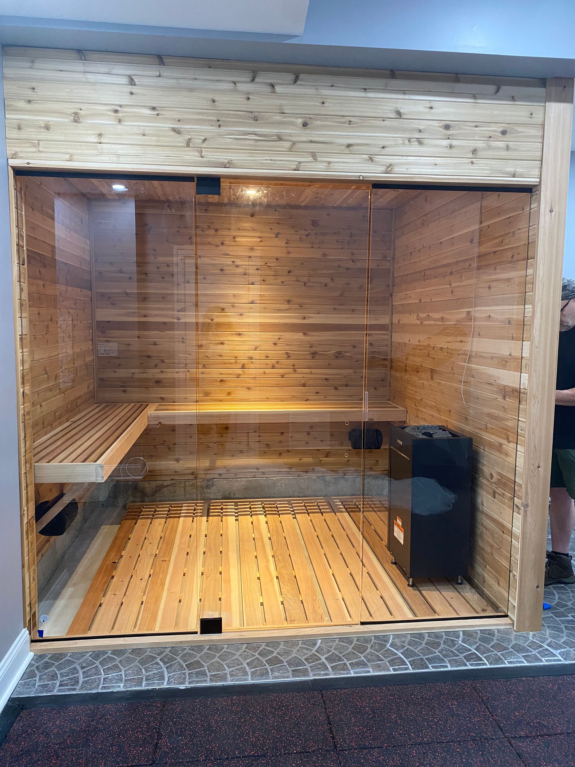 Wood-paneled sauna with benches, warm lighting, and a glass front opening
