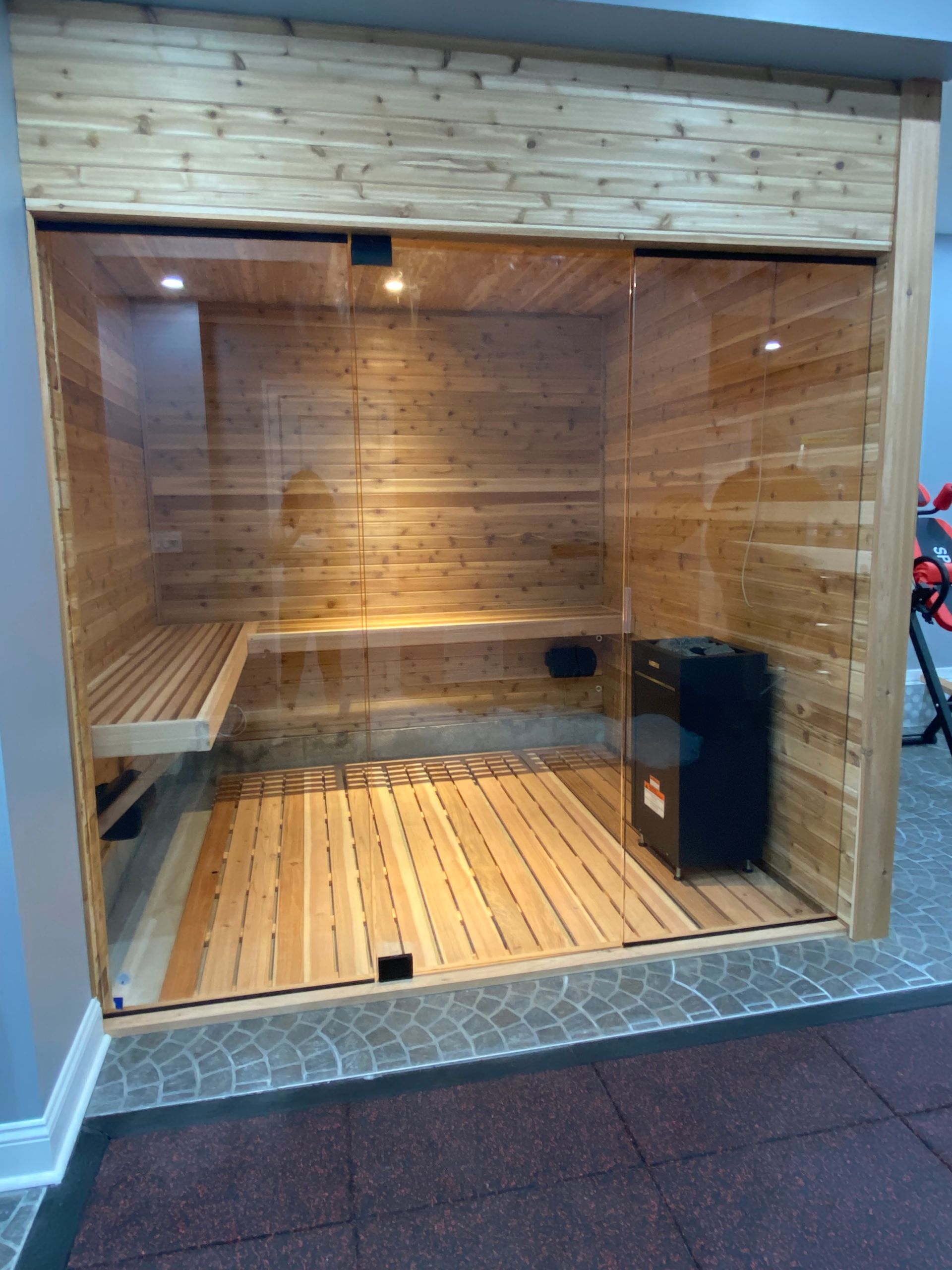 Wood-paneled sauna with benches, wooden slatted floor, and glass front in an indoor setting