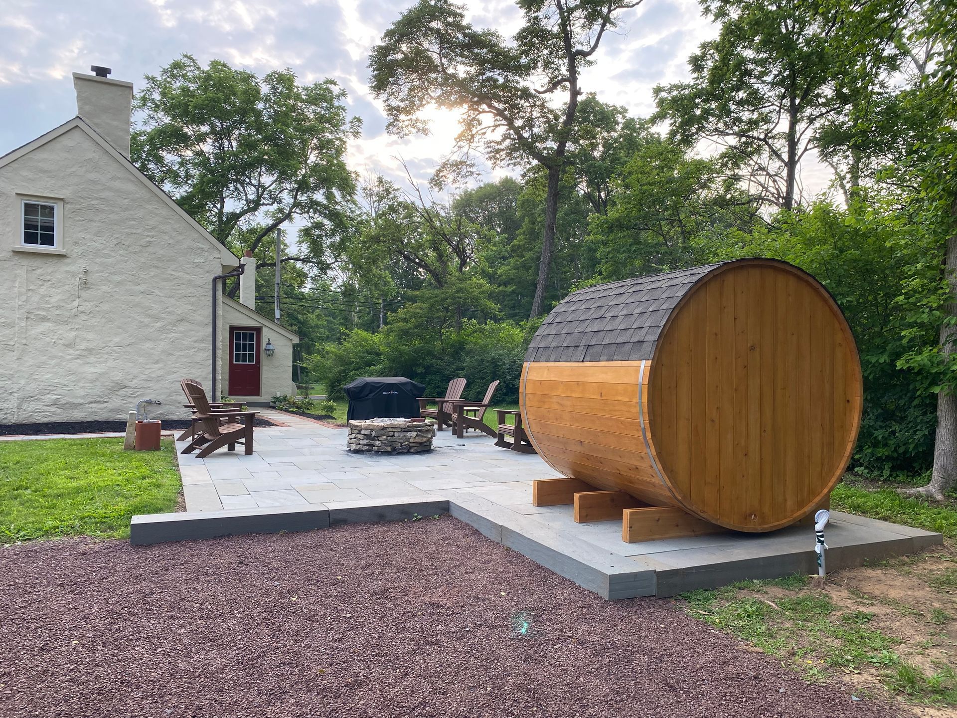 Backyard with a wooden barrel sauna on a patio beside a house and fire pit