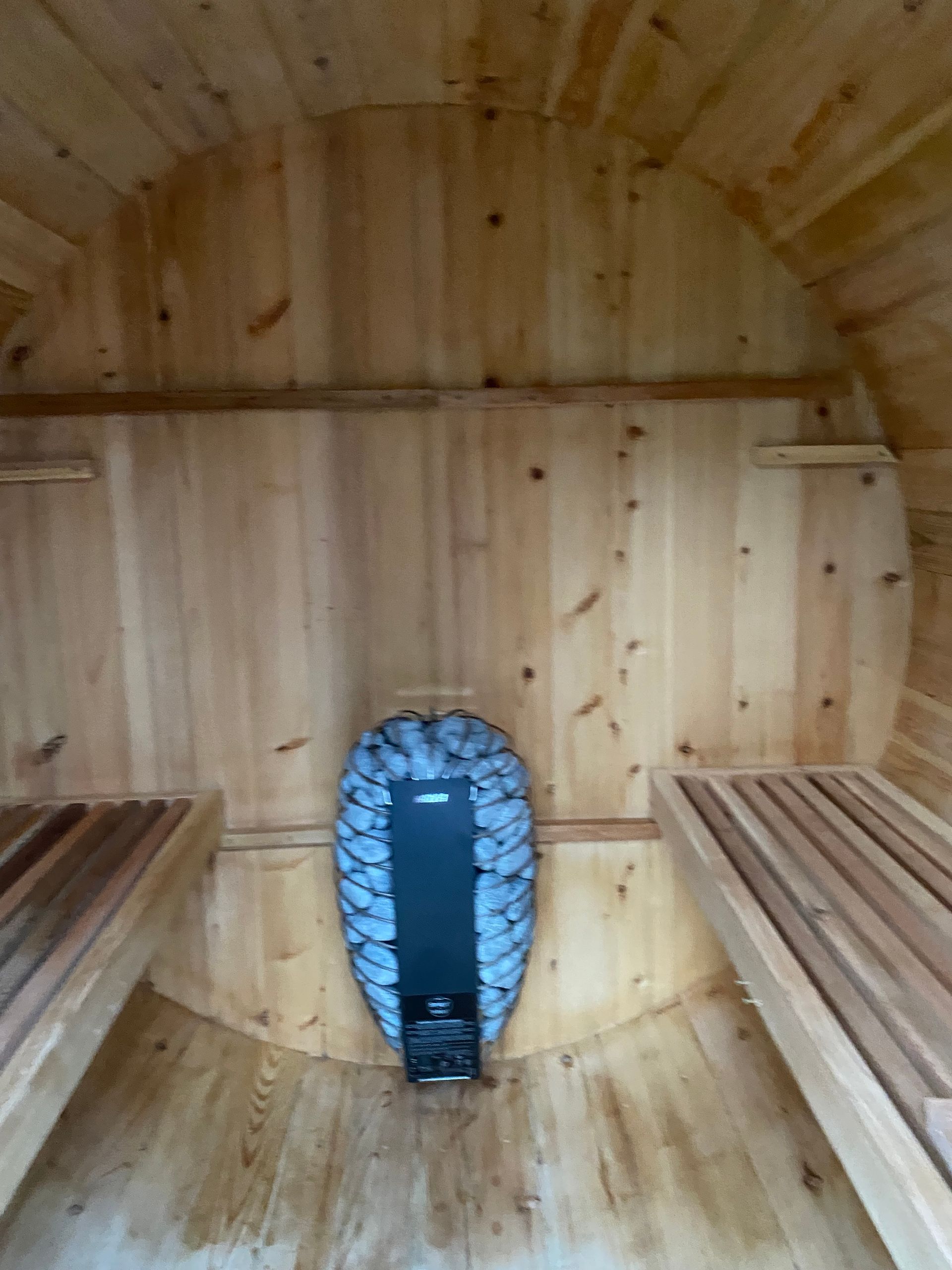 Wooden sauna interior with benches and a stone heater centered against the back wall.