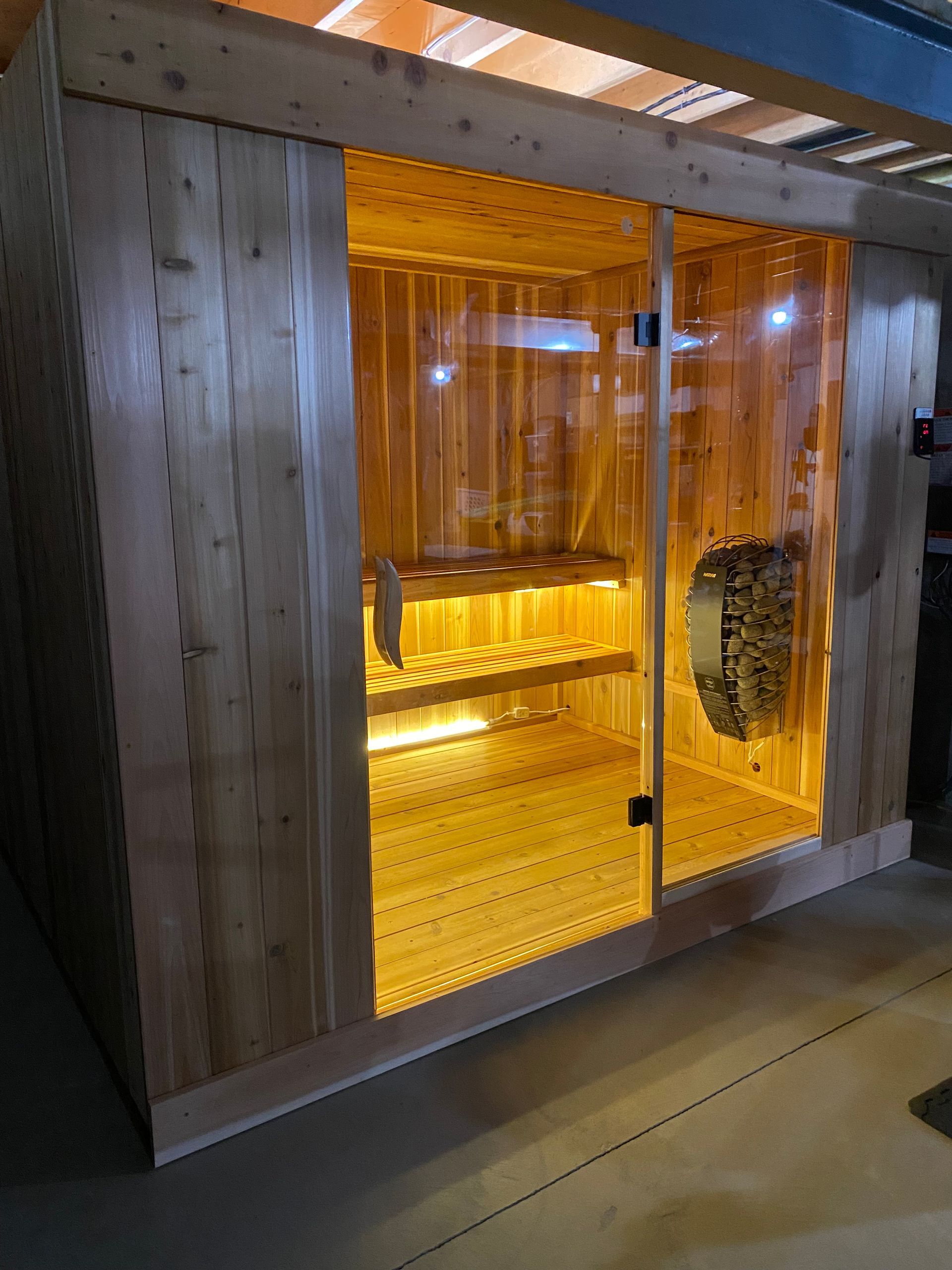 Wood-paneled sauna with warm amber lighting and glass doors in a hallway