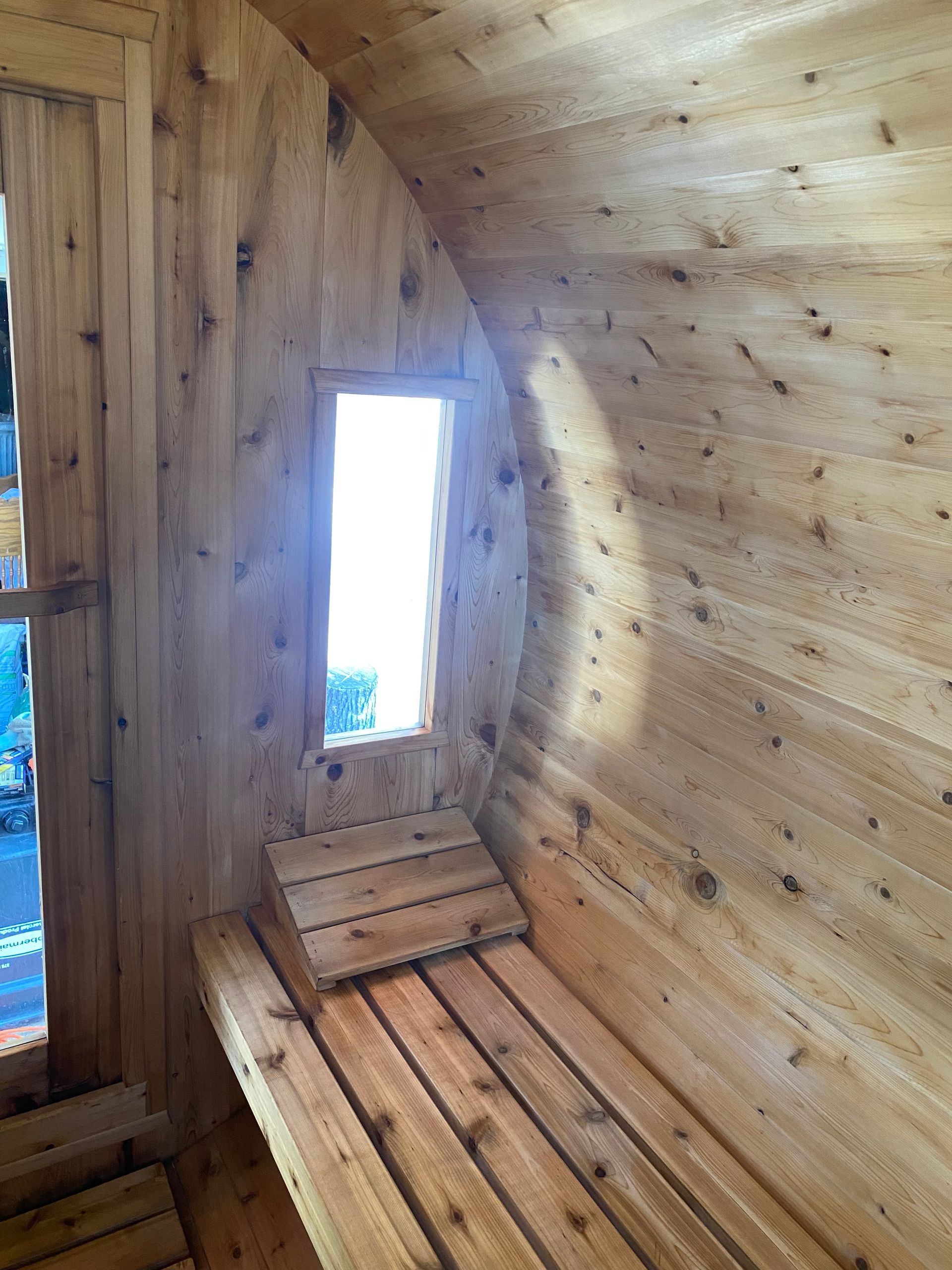 Wooden sauna interior with slatted bench, narrow window, and sunlit plank walls