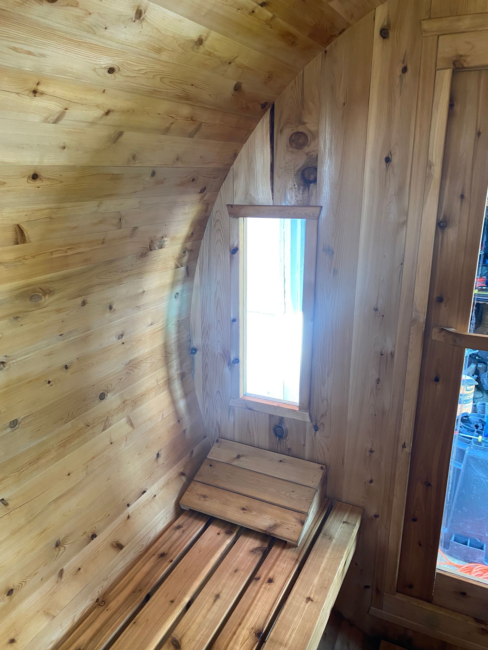 Wooden interior with a narrow bench and small window beside a door opening outside.