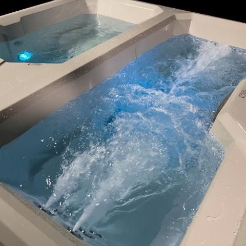 Blue water swirling in two connected indoor hot tubs with white tile walls