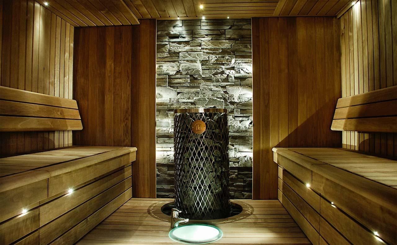Wood-paneled sauna with wooden benches and a central stone heater under warm lighting.