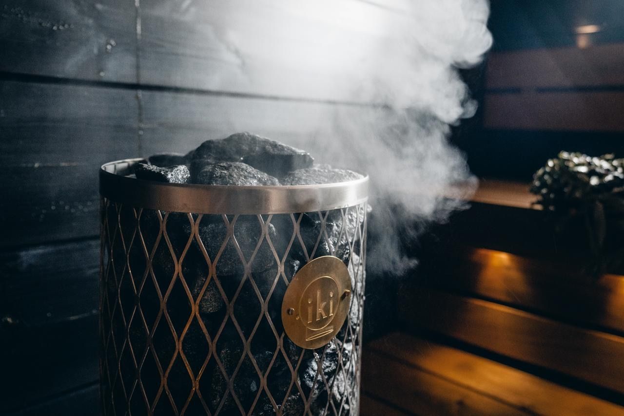 Metal bucket with steaming coals on a wooden table in a dimly lit sauna-like room