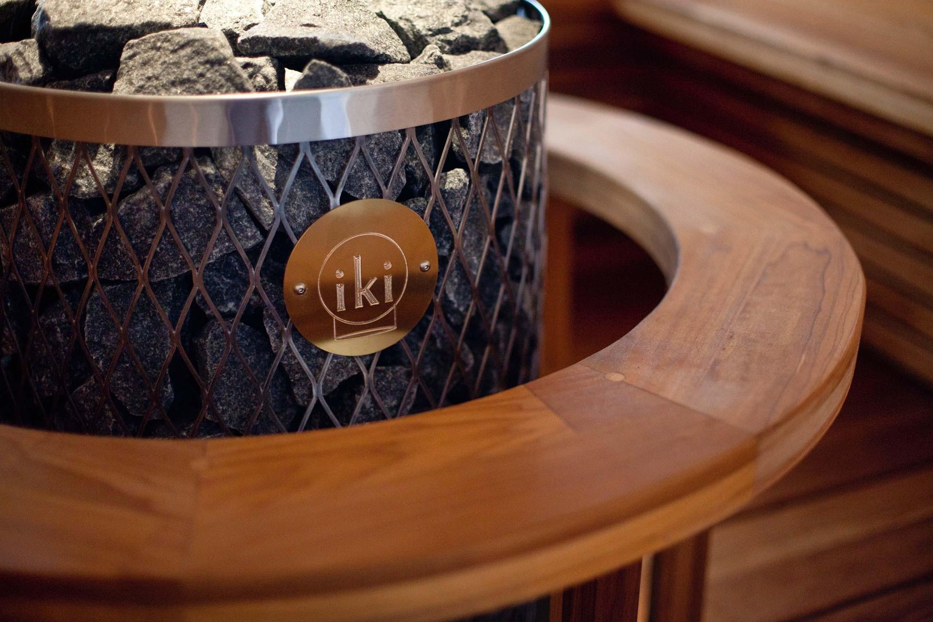 Close-up of a black diamond-patterned candle with a gold label on a wooden tray, topped with stones.