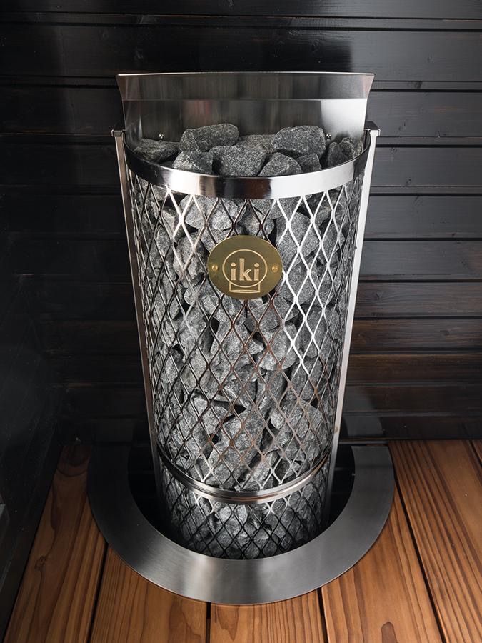 Metal mesh wine cooler filled with charcoal beside a dark wood wall, on a round silver base.