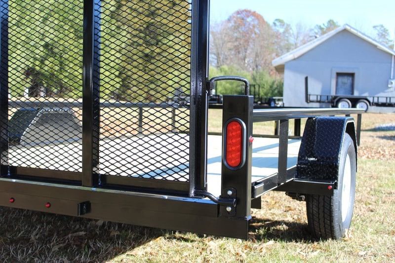 Black mesh utility trailer with red reflectors parked on grass near a white house.
