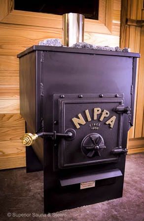 Black Nippa wood stove with metal door and chimney pipe indoors, against a wooden wall.