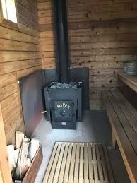 Black Nippa wood stove with metal door and chimney pipe indoors, against a wooden wall.