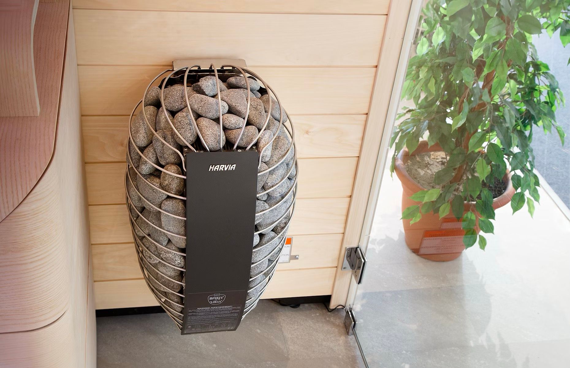 Tall black mesh heater in front of a stone planter beside a potted plant on a patio.