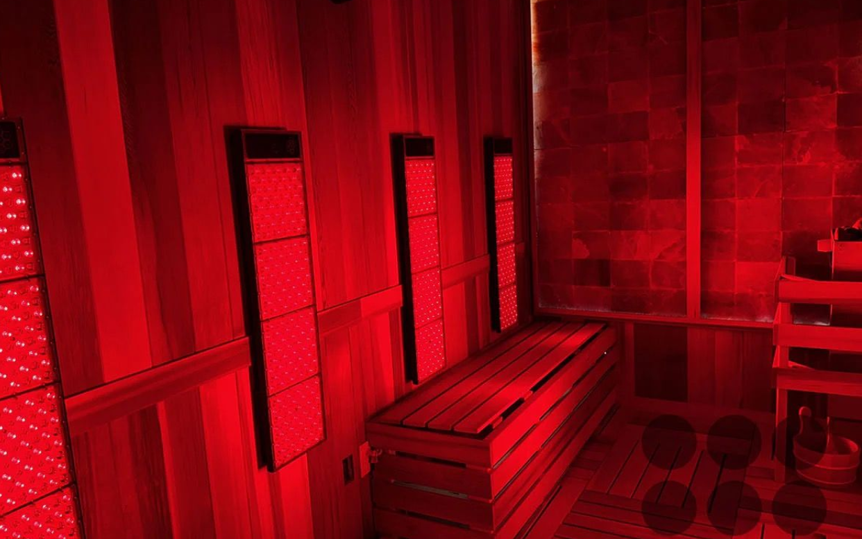 Red-lit sauna room with wooden benches, towels, and buckets.
