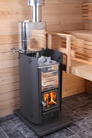 Black sauna stove with metal flue in a wooden sauna room, on a gray floor mat.