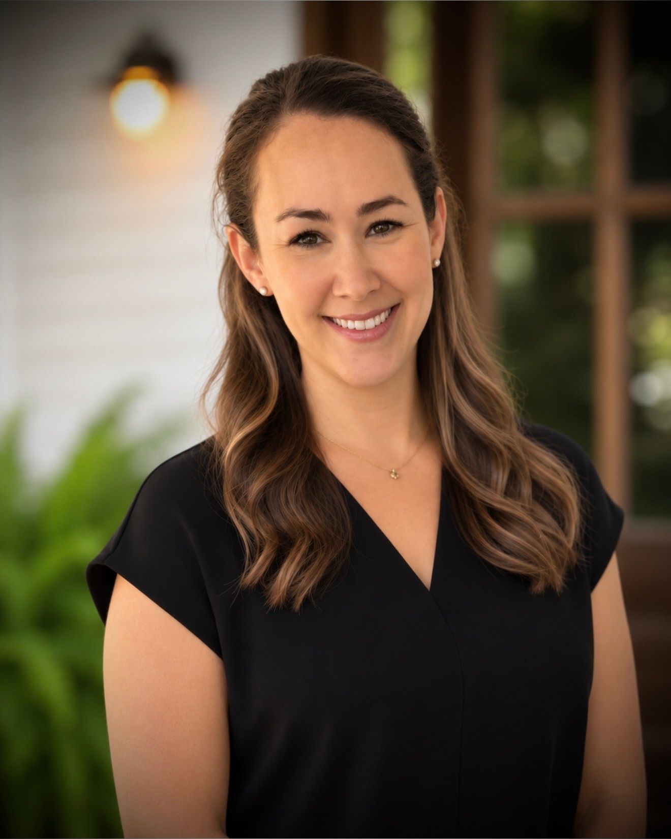 Smiling woman in a black blouse standing outdoors by a porch with a blurred house background