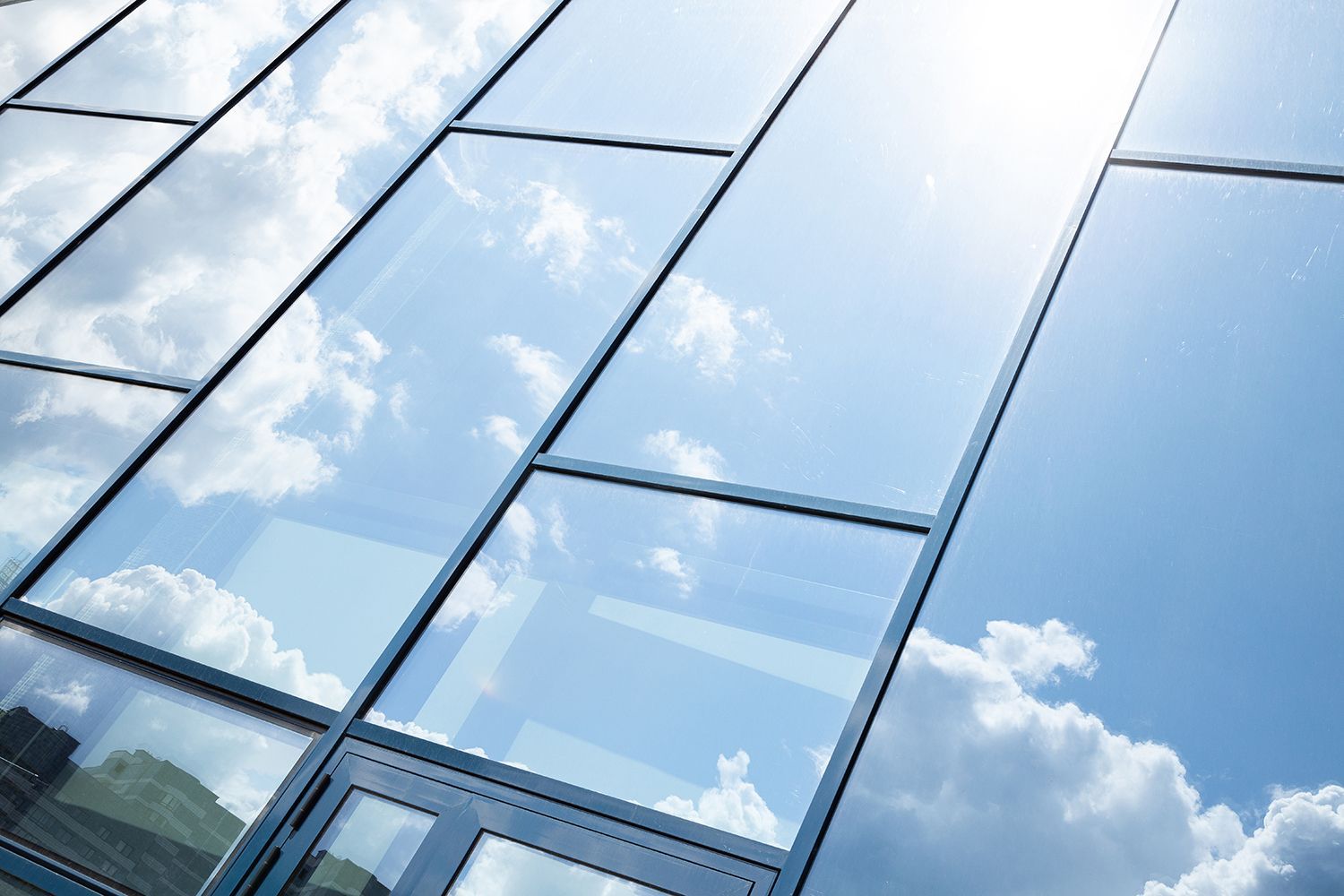 Close-up of the glass window facade of a building, showing the reflection of the sunny sky. Close-up of the glass window facade of a building, showing the reflection of the sunny sky.