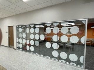Glass wall with white circular designs, leads to waiting area with seating.