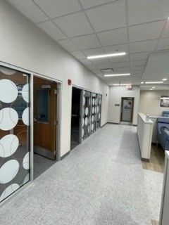 Hallway with offices, white walls, speckled floor, glass doors, and recessed lighting.