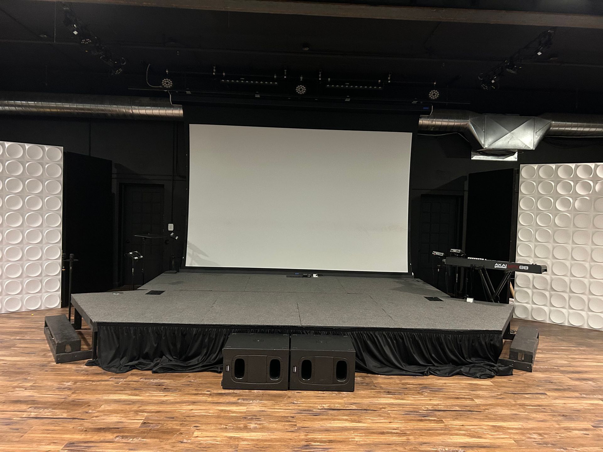 Small empty stage with a blank projection screen and black curtains in a dark venue