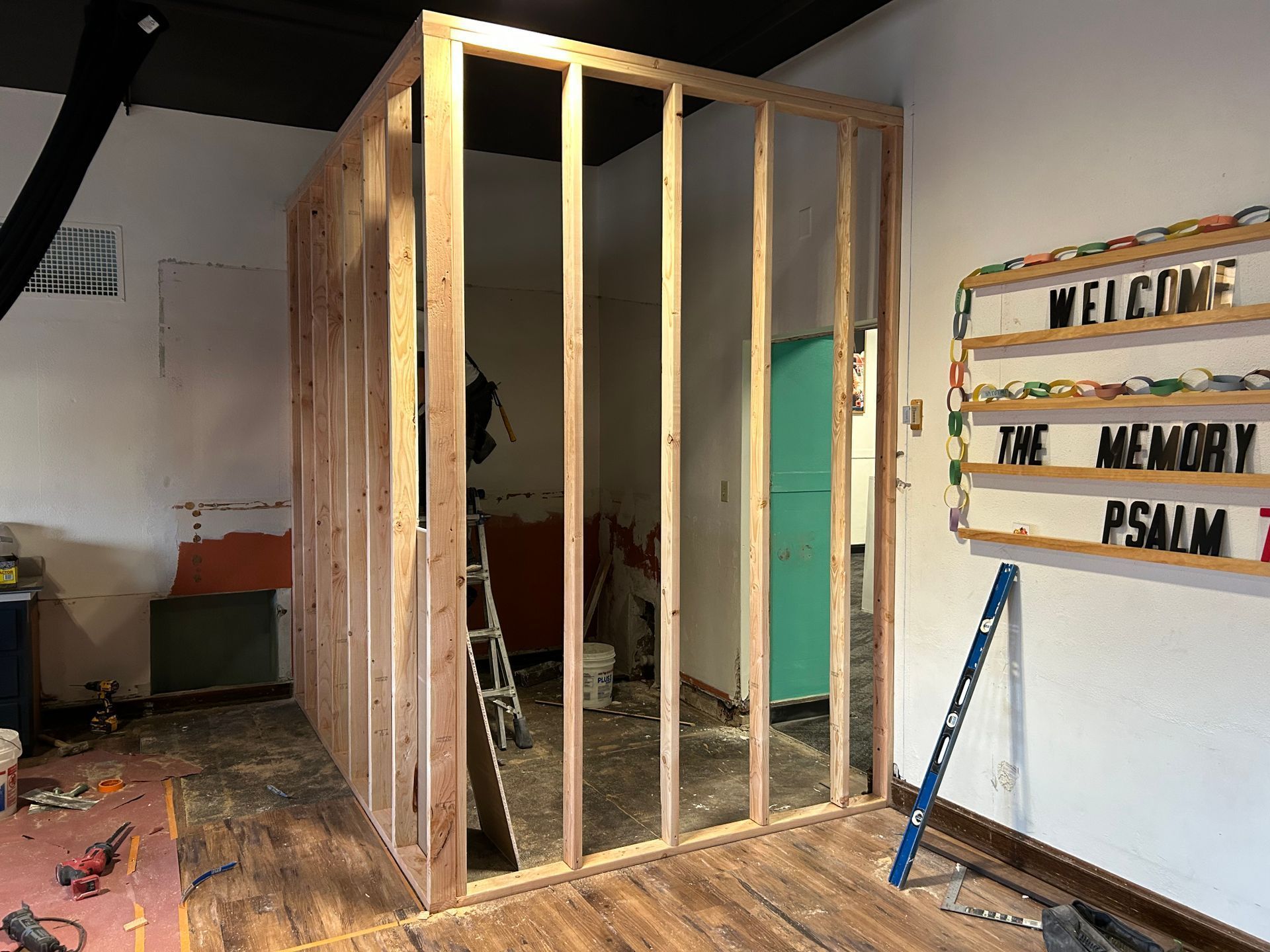 Interior under construction with framed wooden wall, tools, and a welcome sign on the right.
