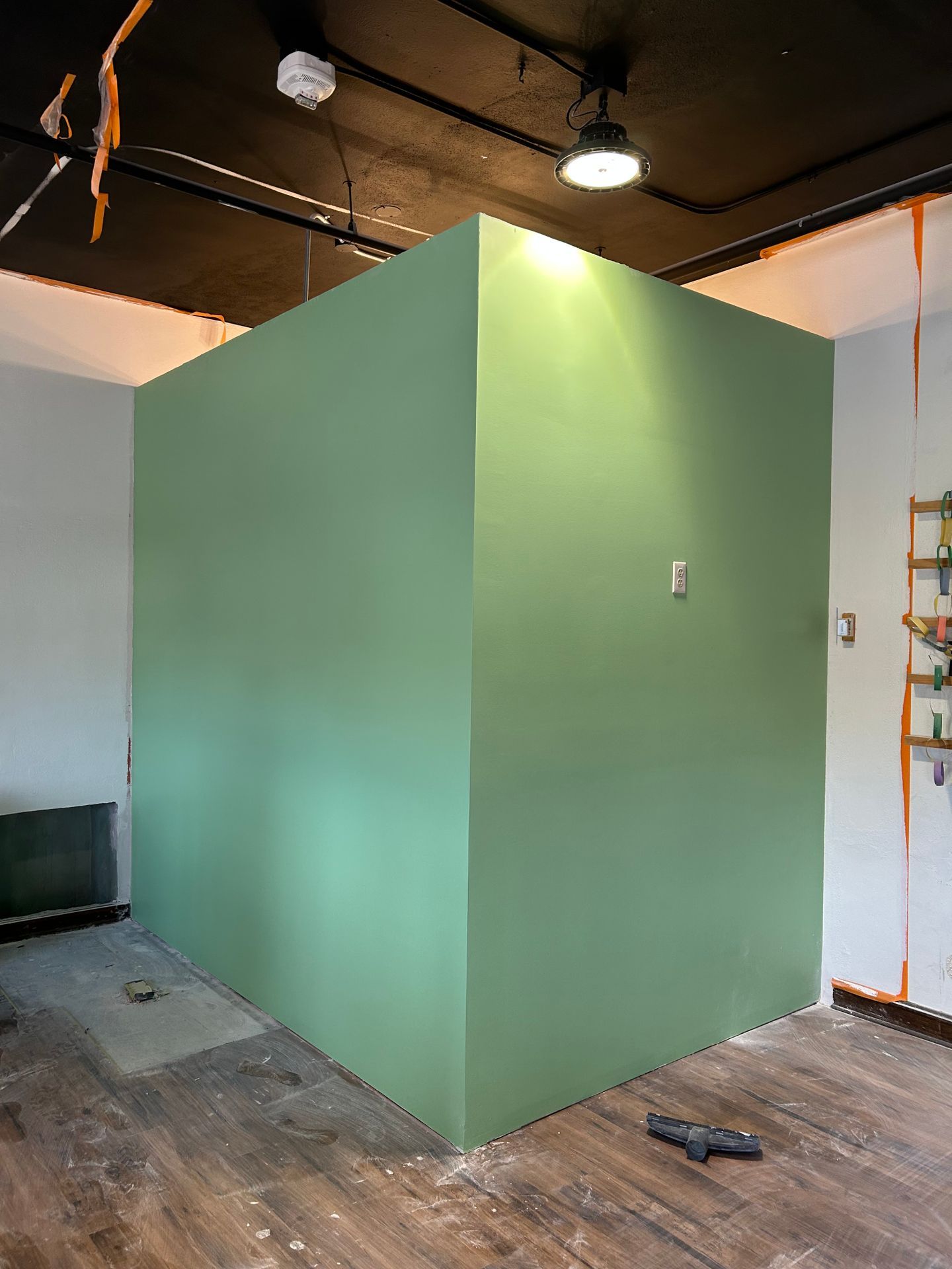 Green partition wall in an unfinished room with exposed ceiling and wood floor.