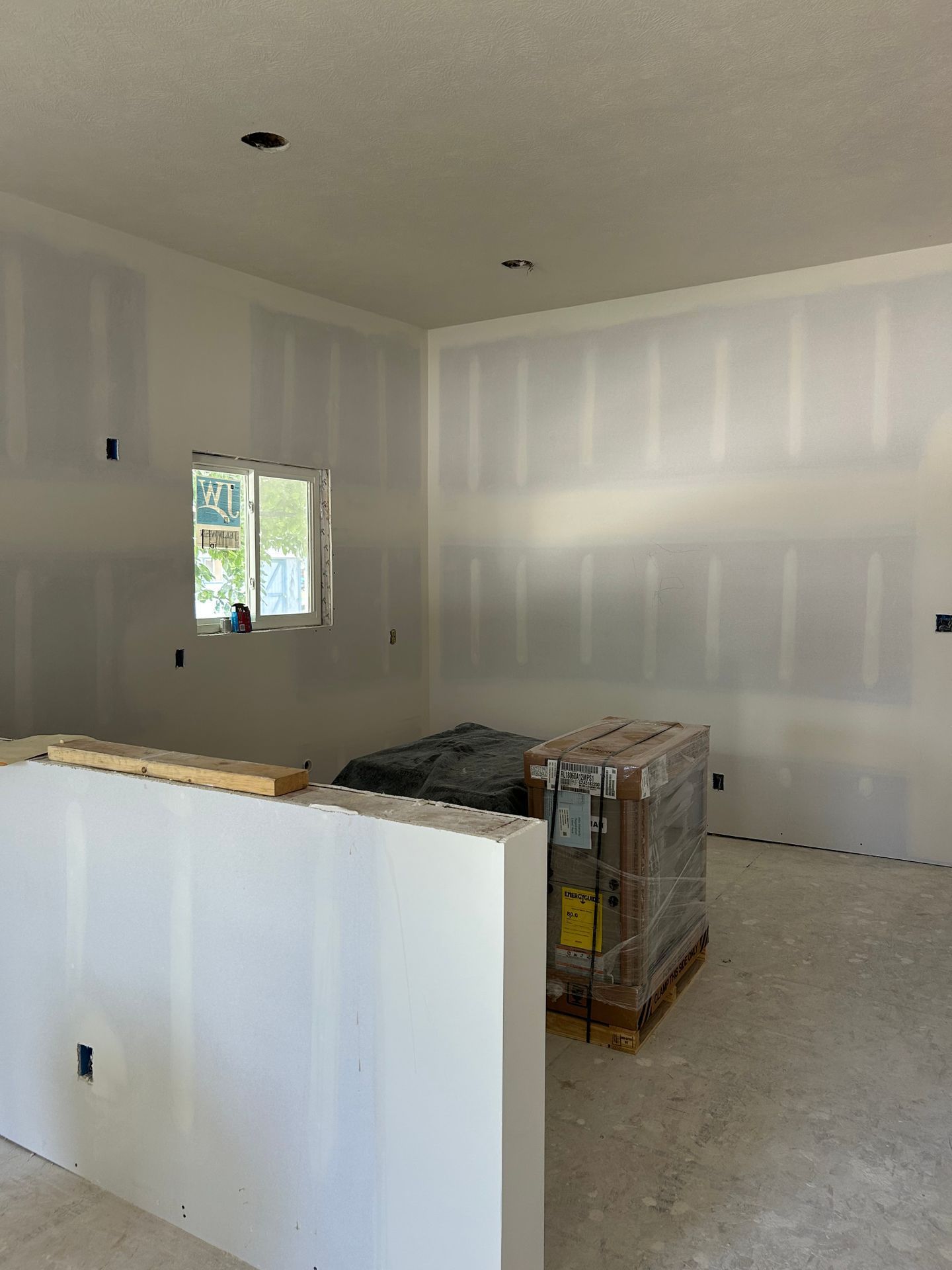 Unfinished room with drywall, small window, and construction materials on the floor
