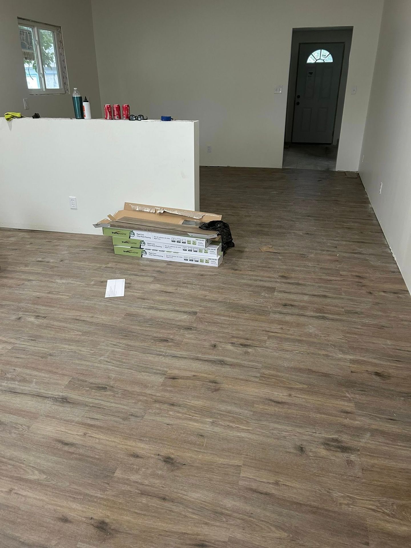 Empty room with wood-look flooring, a white half-wall, and boxes near a doorway.