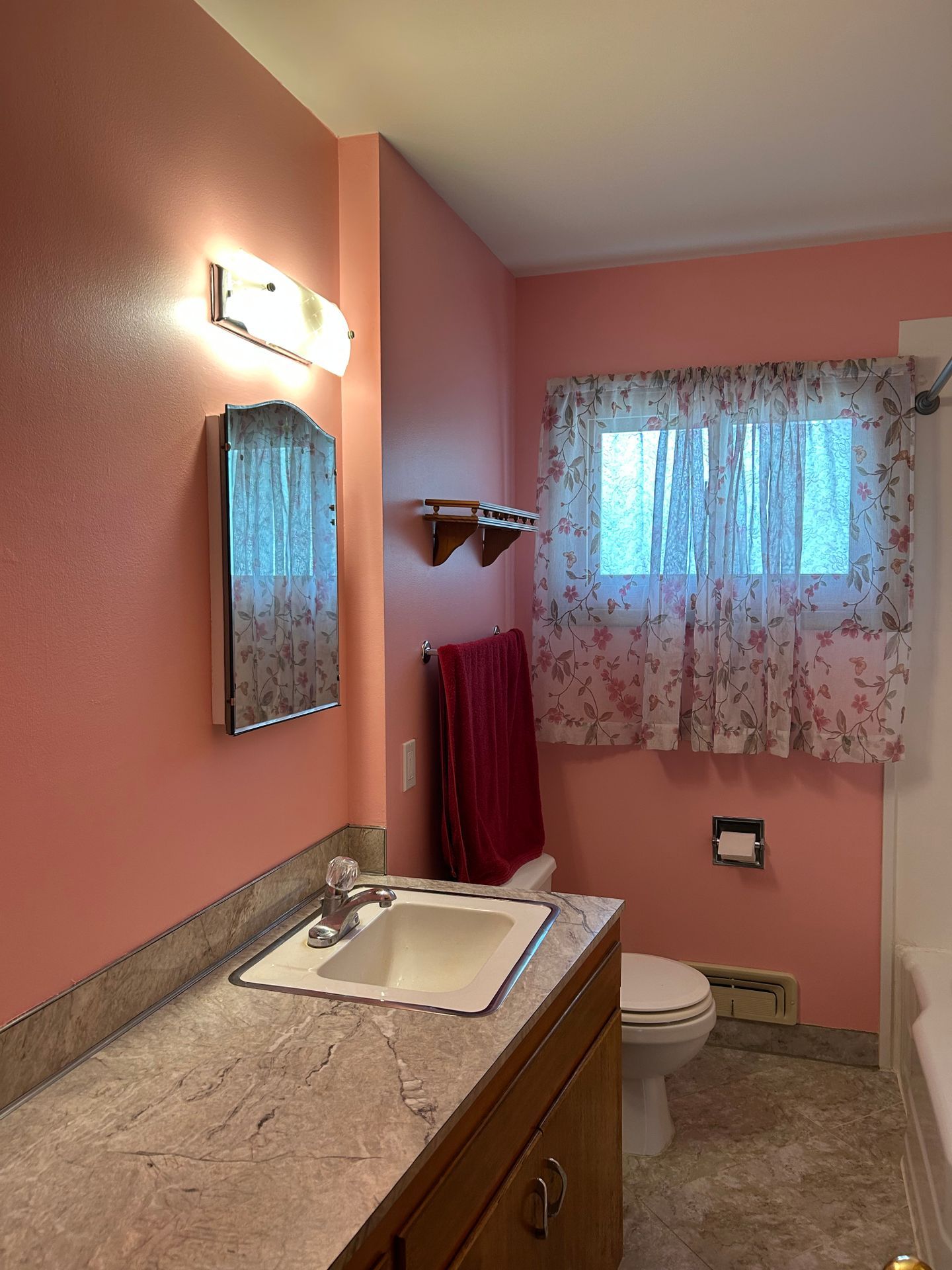 Small bathroom with pink walls, granite vanity, mirror, window curtain, and toilet.