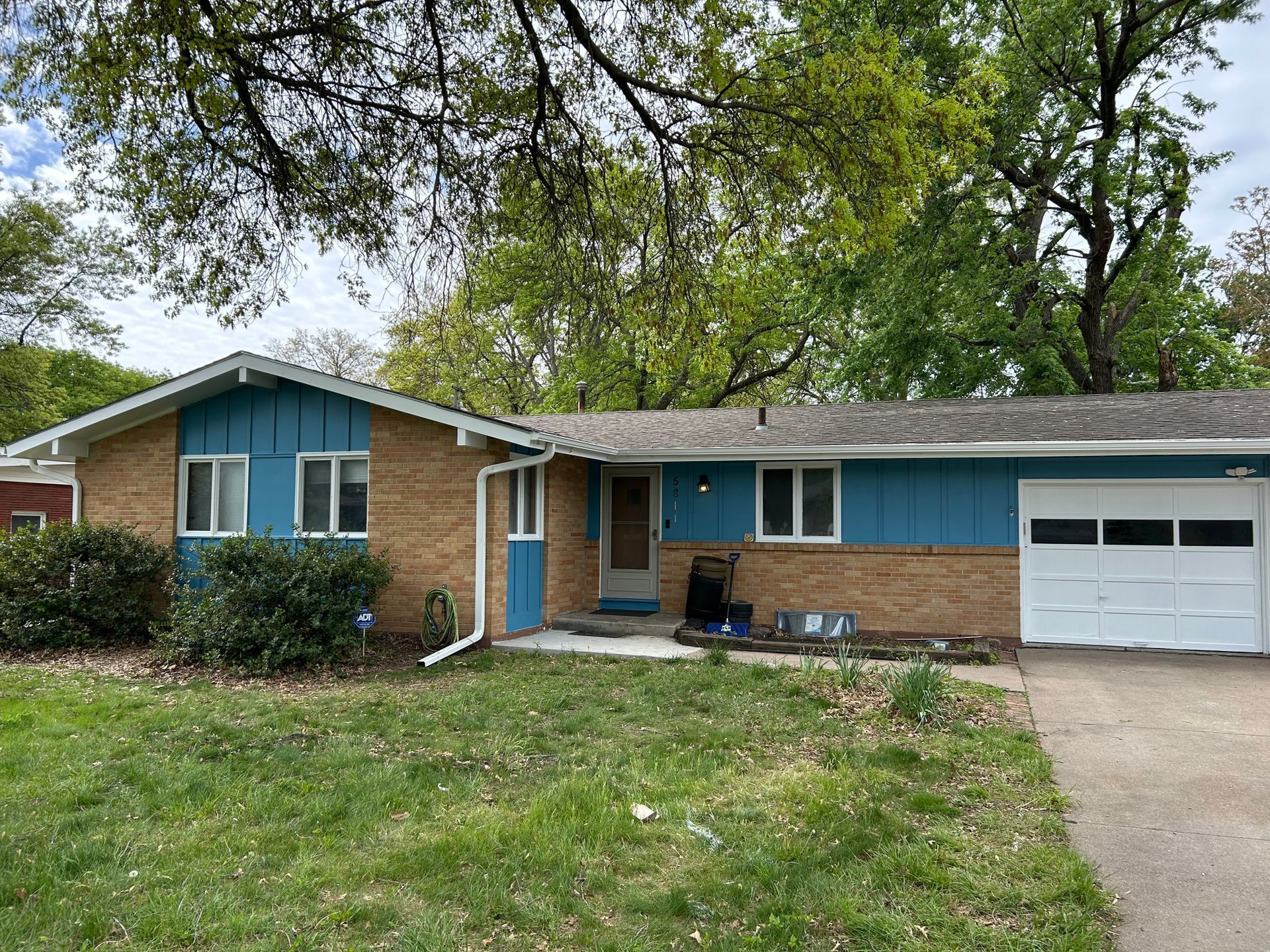 Single-story brick house with blue trim, garage, and front lawn under trees