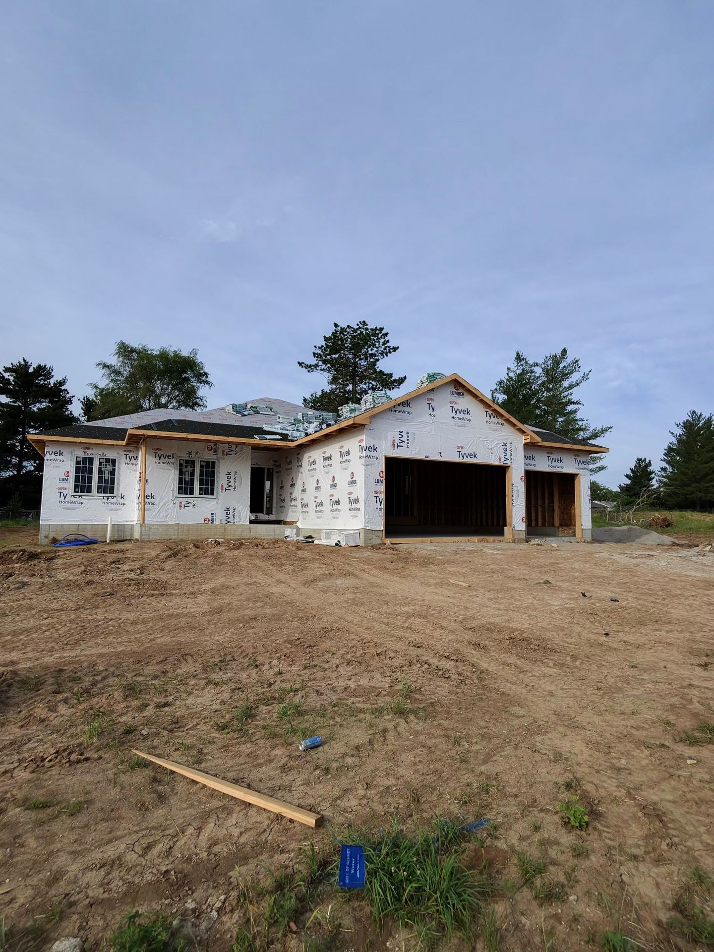 Partially built house with white siding and open garage on a bare dirt lot under a cloudy sky