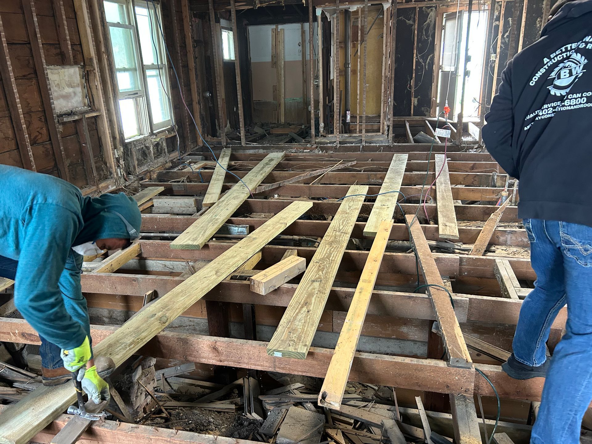 Workers installing floor joists in a gutted house interior during renovation