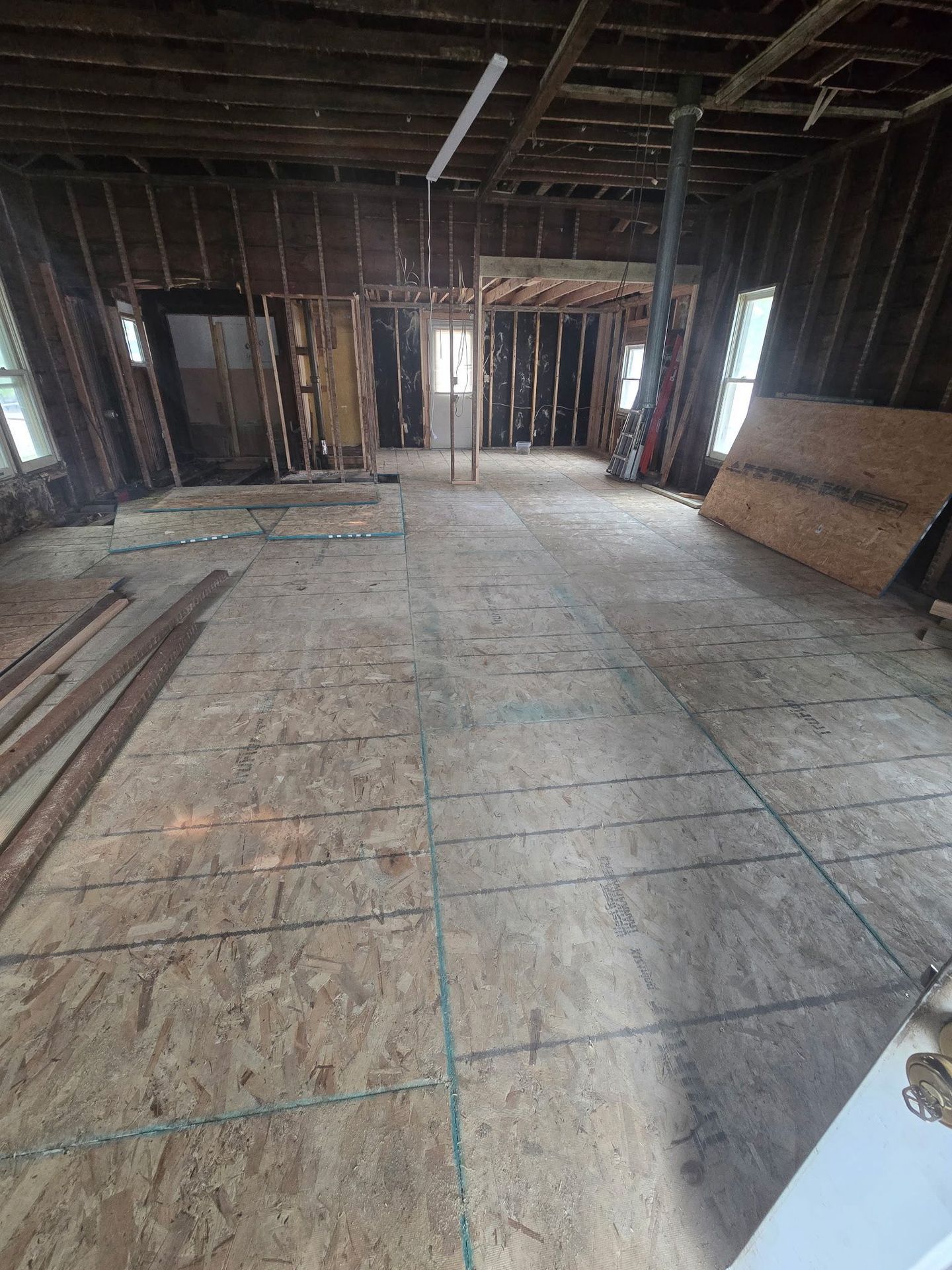 Partially renovated house interior with exposed framing, plywood subfloor, and stacked boards