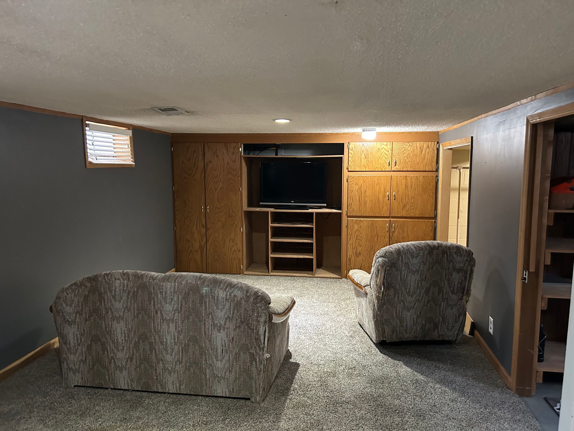 Basement family room with two recliners, wood cabinets, and a TV nook at the far wall