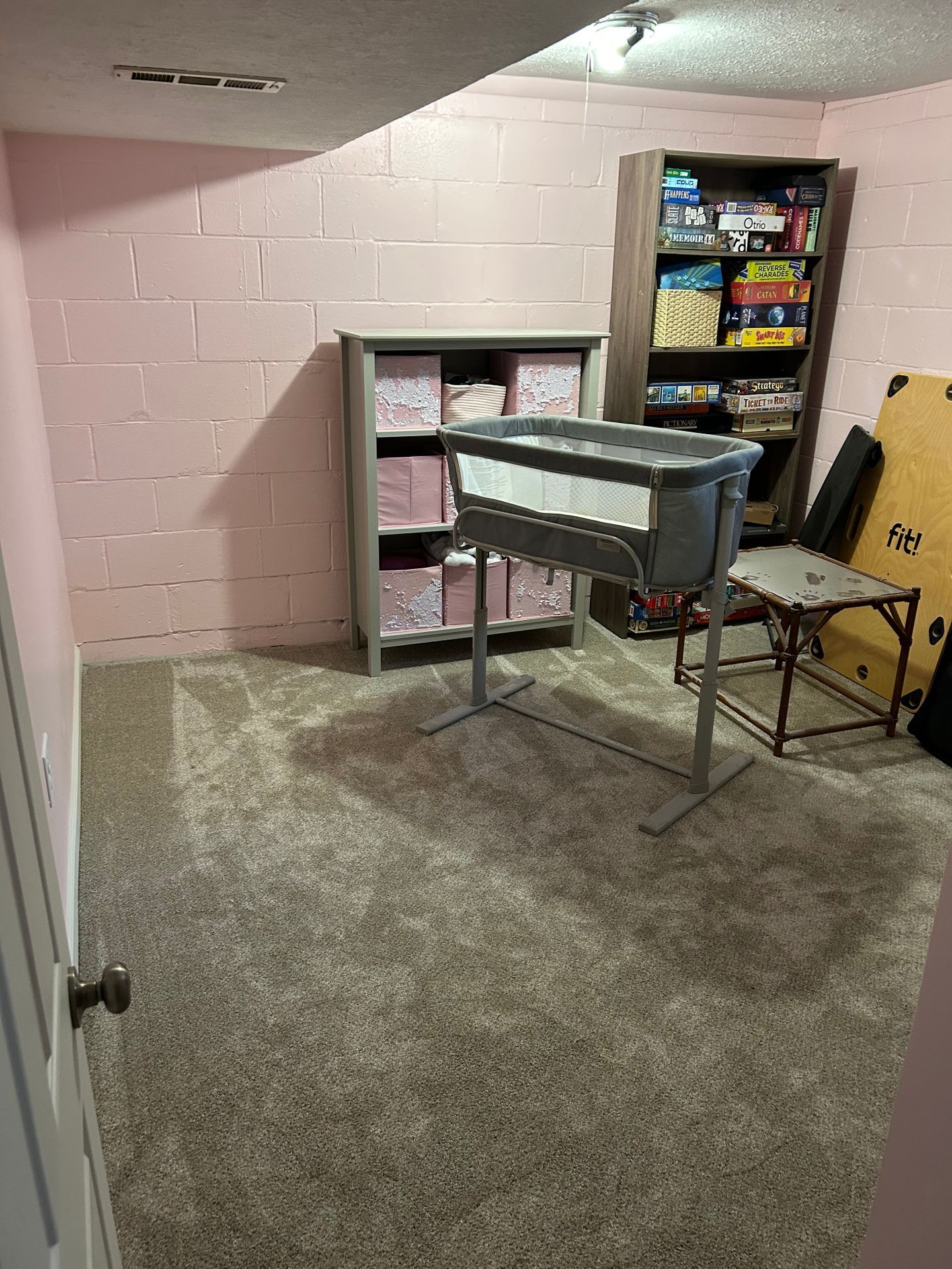 Basement nursery with pink walls, carpet, crib, changing table, and shelving unit.