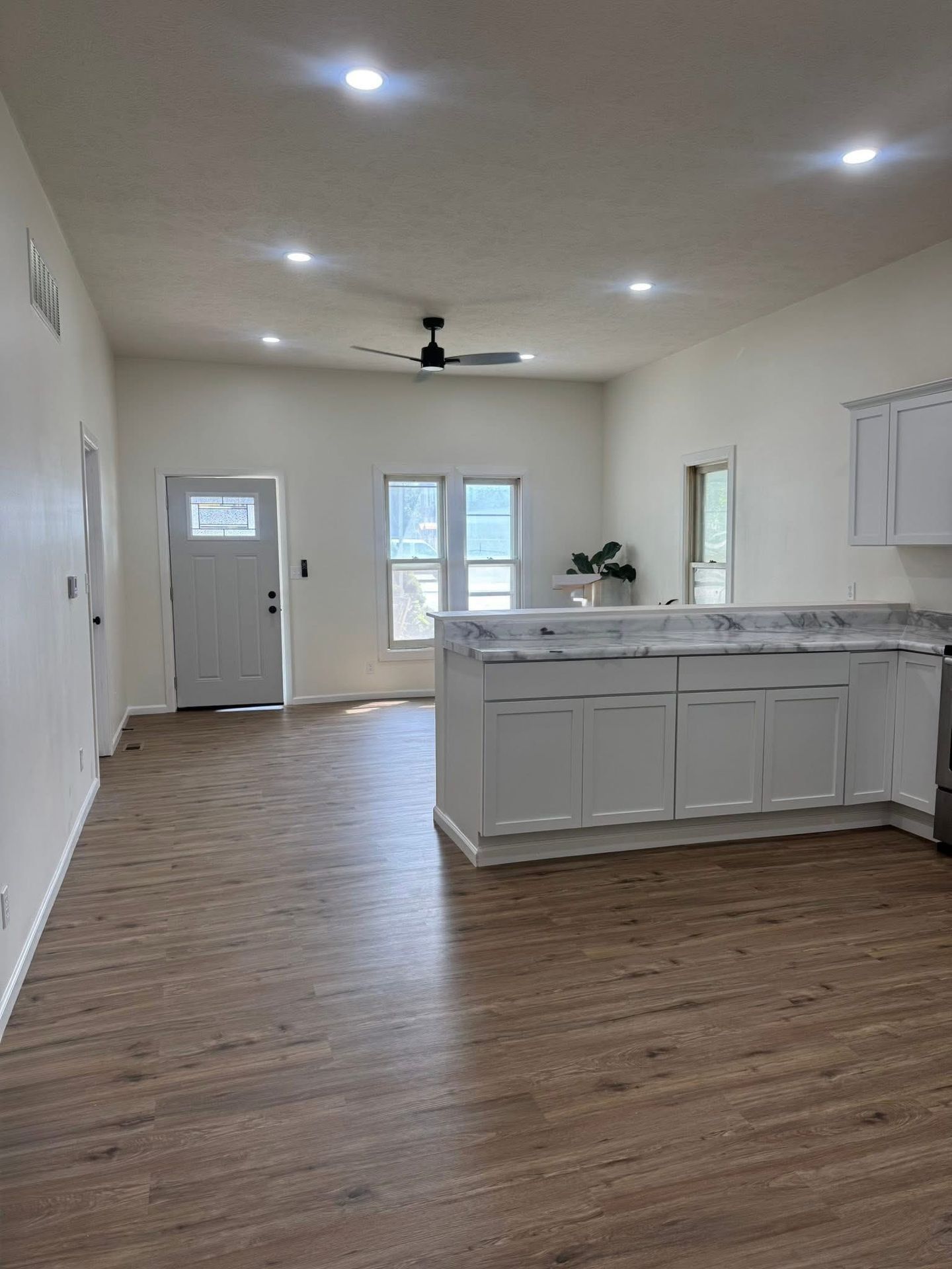 Bright open kitchen with white cabinets, wood floors, island, and ceiling fan