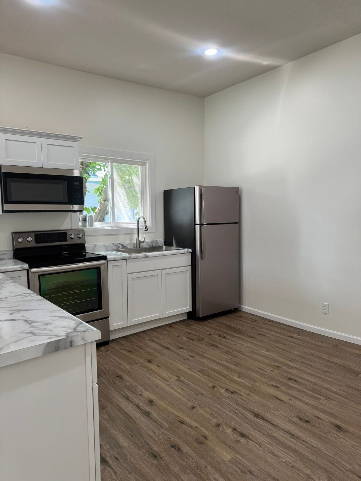 Empty modern kitchen with white cabinets, stainless appliances, gray fridge, and wood-look flooring