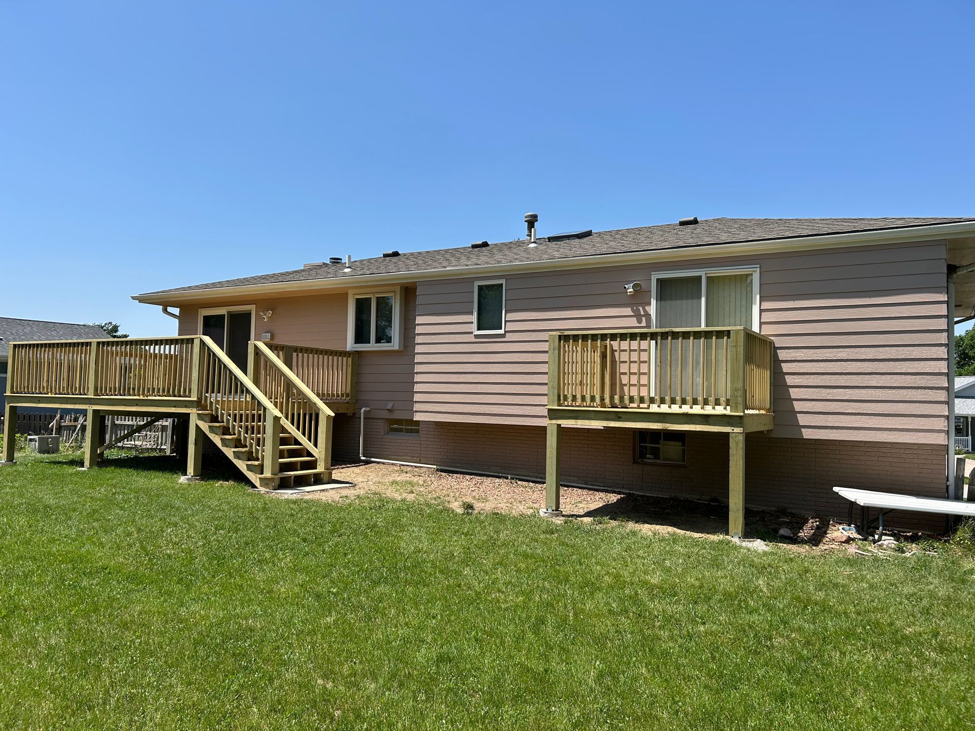 Single-story beige house with a wooden deck and stairs, set in a grassy yard