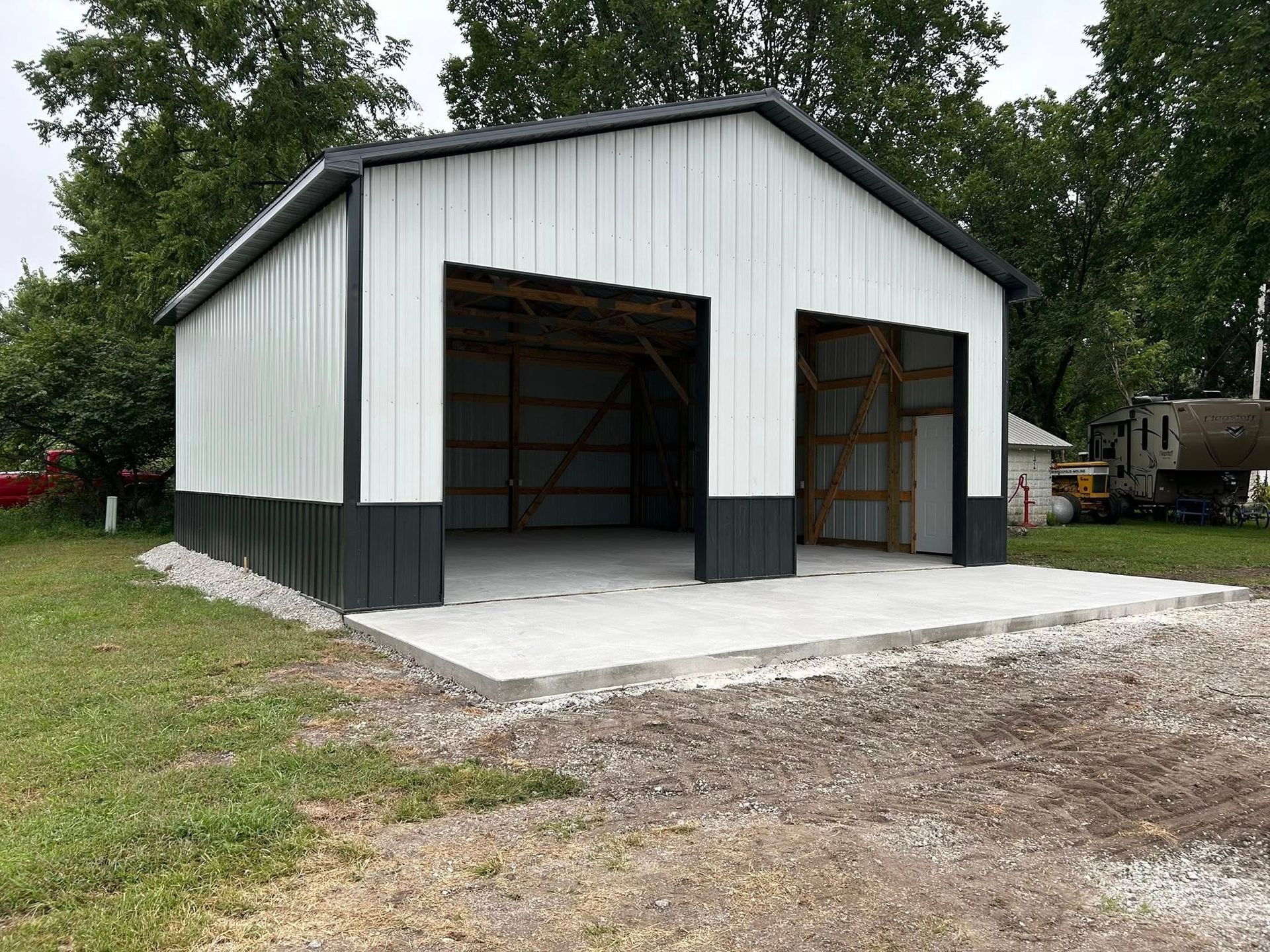 White metal barn-style garage with two open bays and a concrete apron in a grassy yard