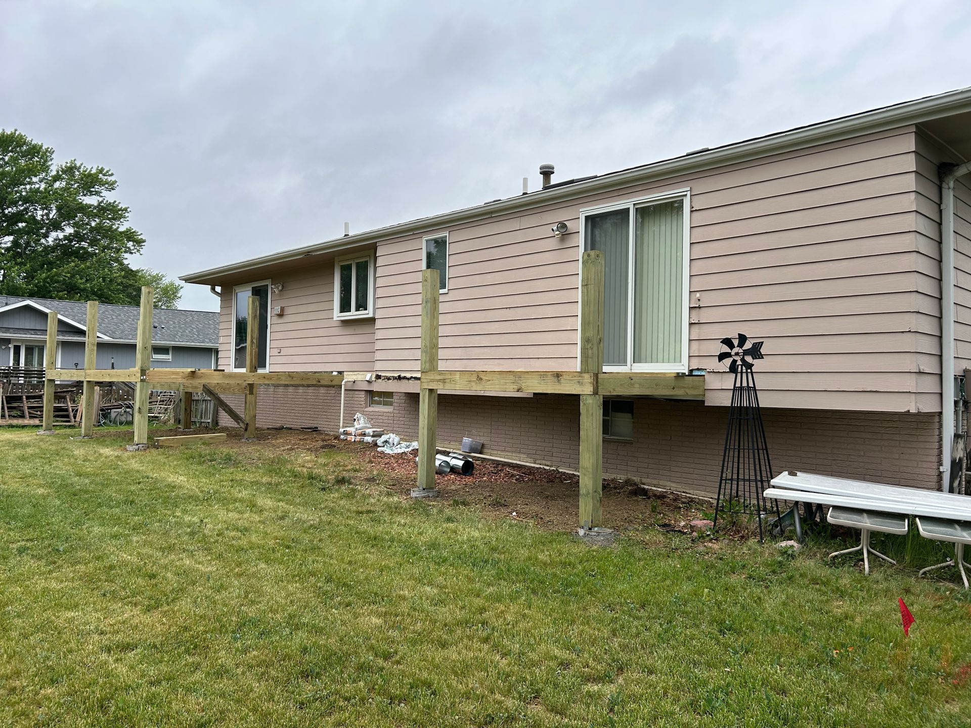 Raised beige house with sliding glass door and wooden deck posts over a grassy backyard