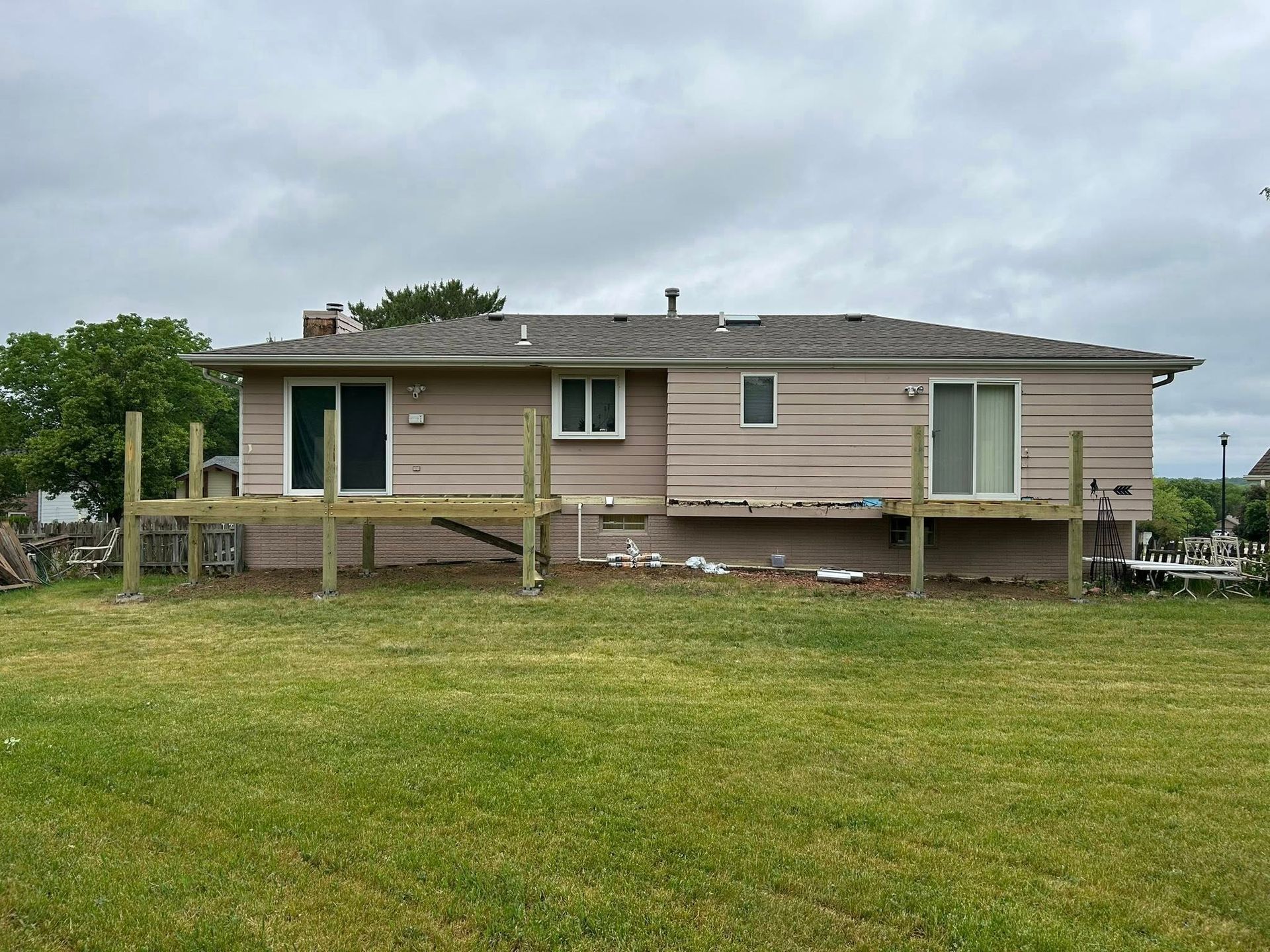 Single-story beige house with a wooden deck in a grassy yard under a cloudy sky
