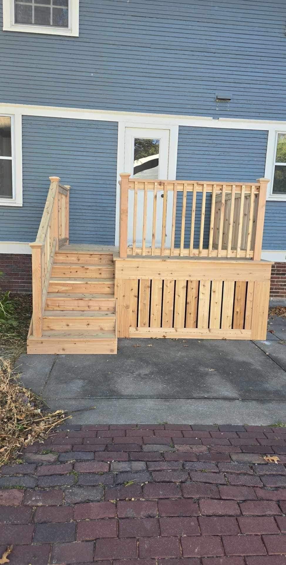 Small wooden front porch and stairs attached to a blue house beside a brick walkway.