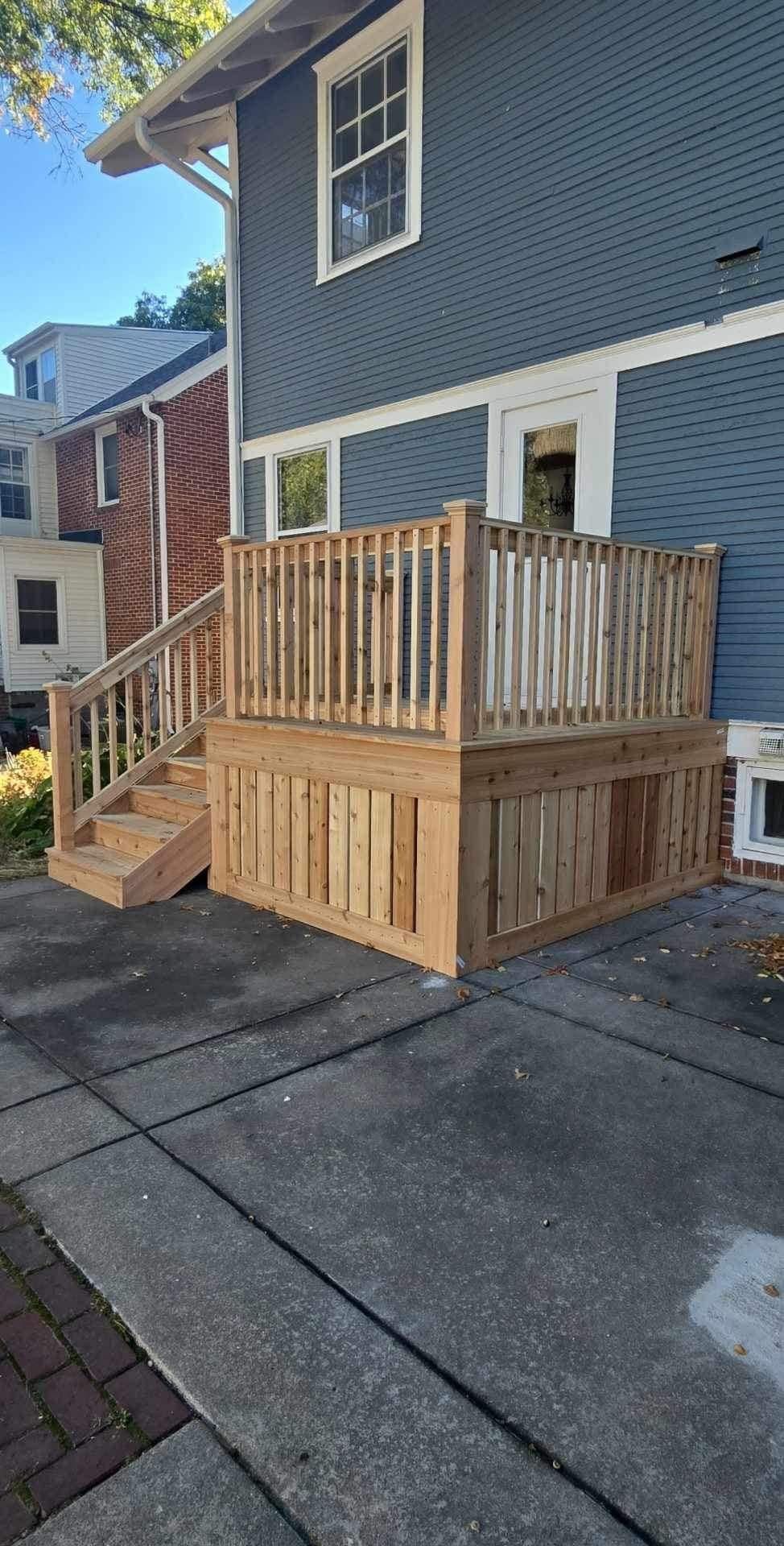 Wooden accessibility ramp and platform attached to a blue house beside a driveway