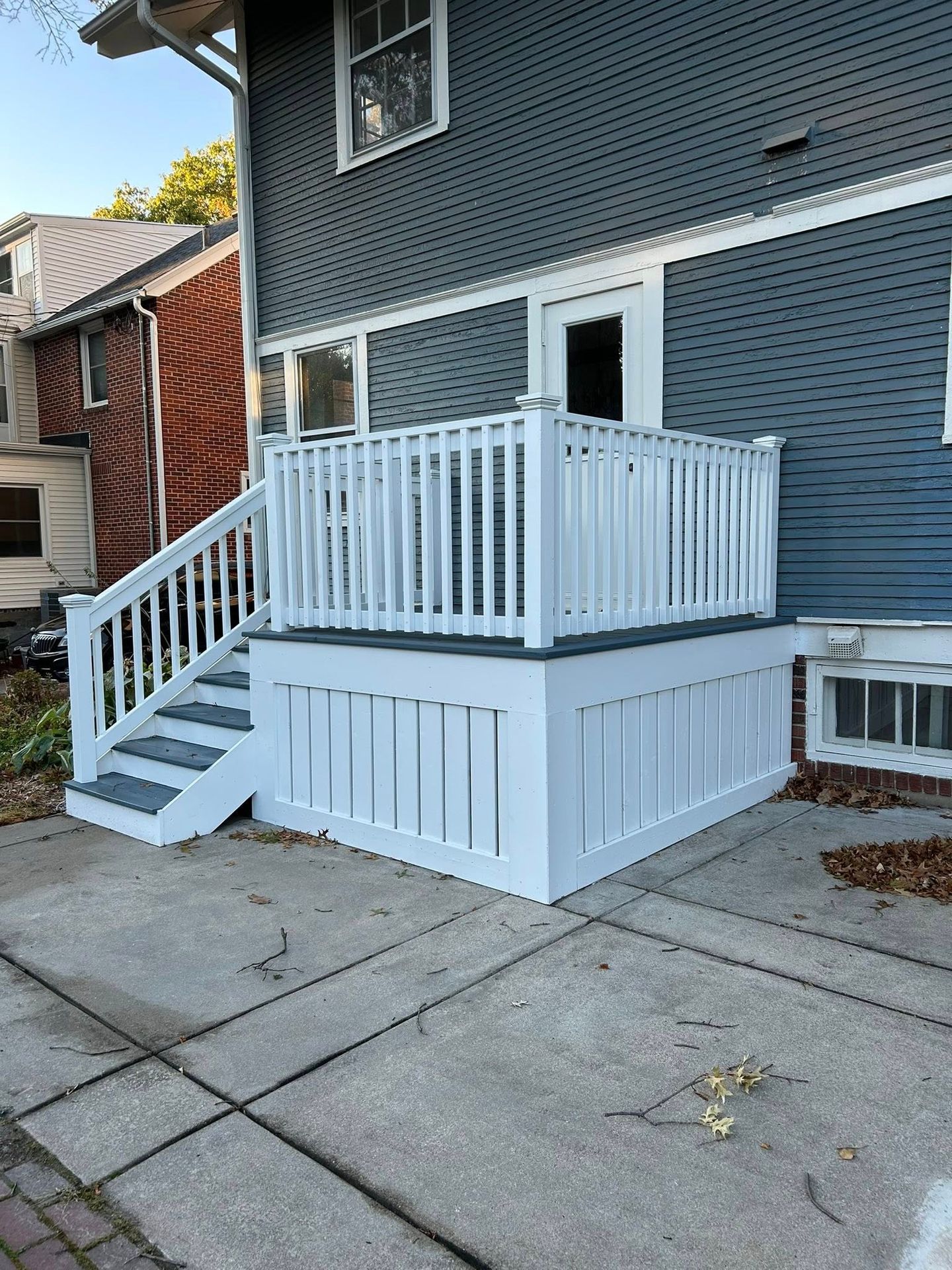 Small white wheelchair-accessible ramp and porch attached to a gray house with stairs.