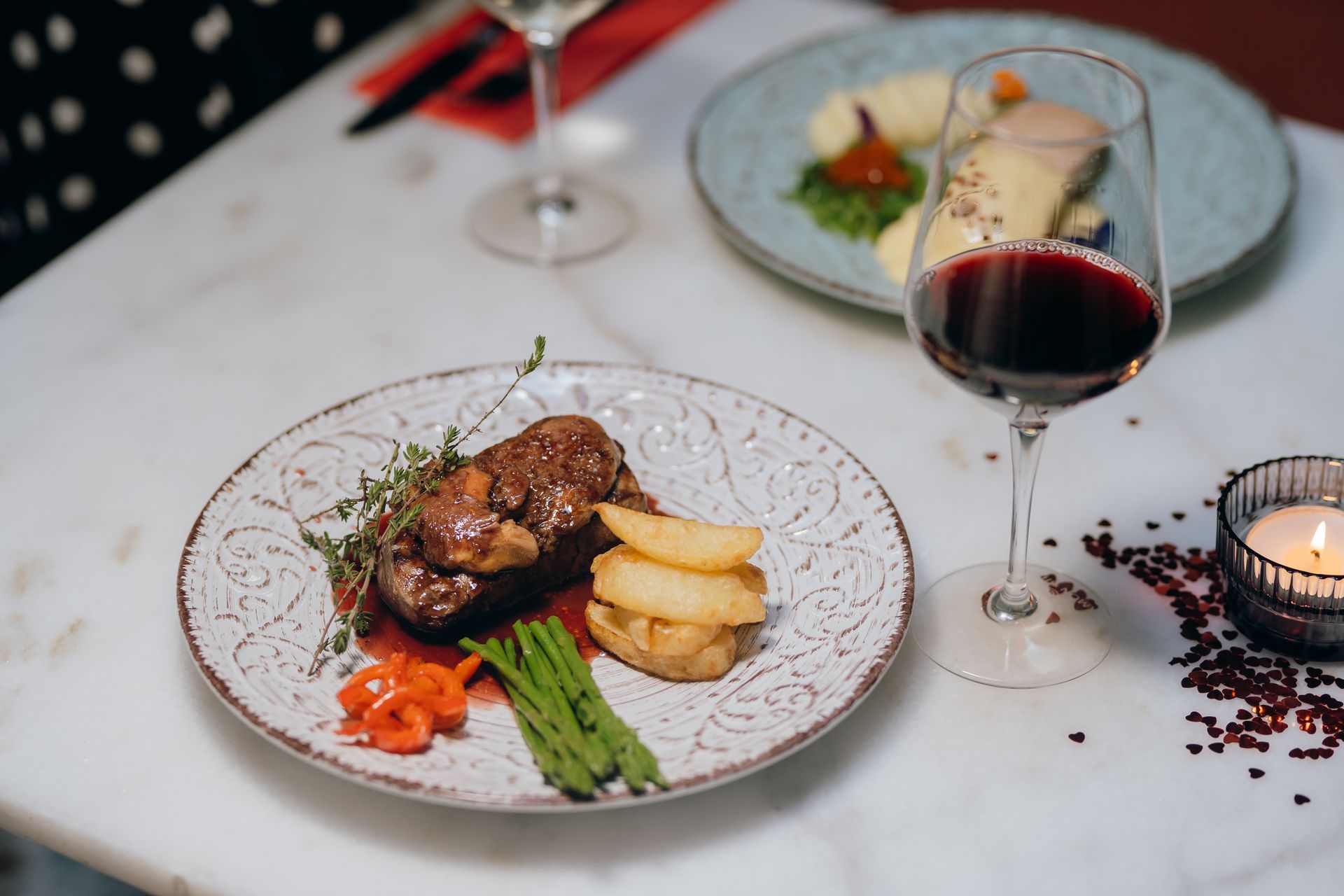 Elegante mesa con filete emplatado, espárragos, patatas y copas de vino tinto a la luz de las velas.