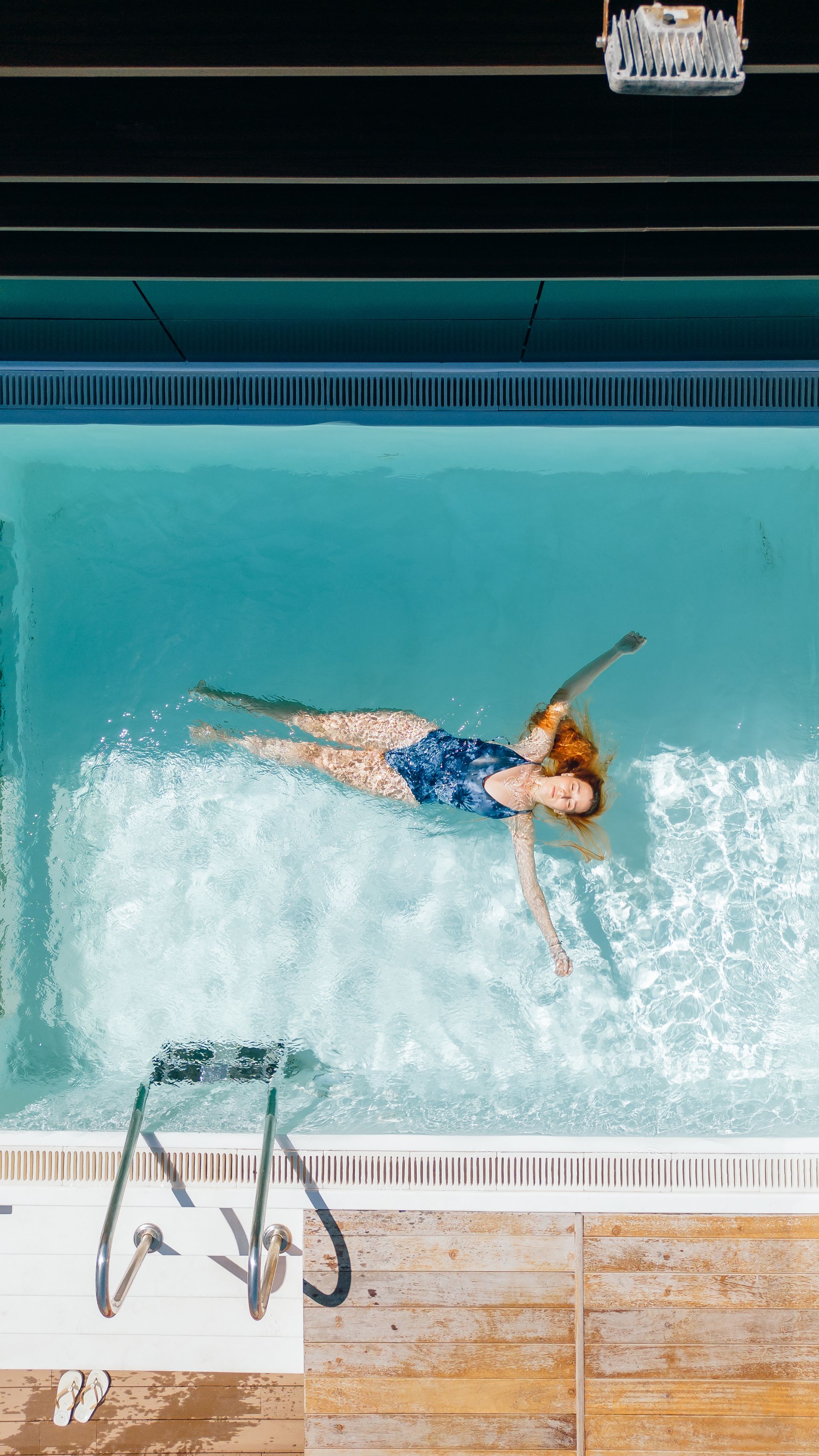 Vista aérea de un nadador en una piscina, flotando de espaldas junto a una escalera de piscina.