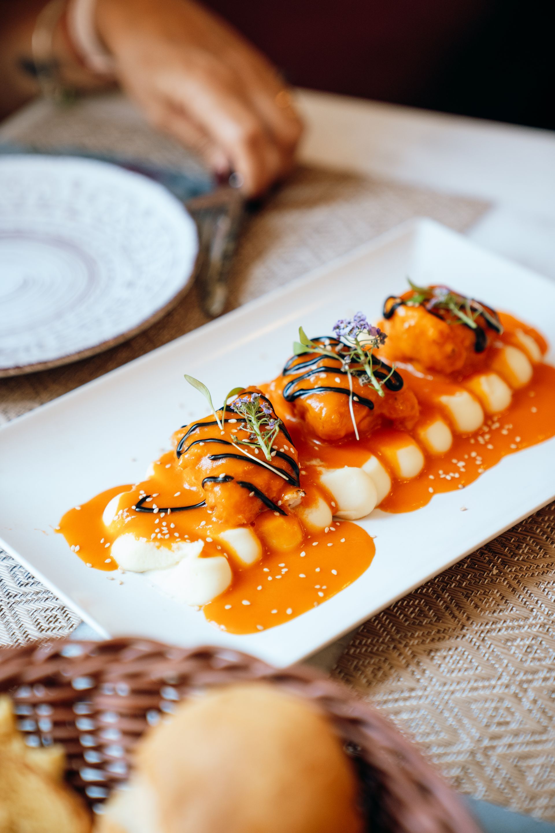 Aperitivo glaseado con naranja y cubierto con hierbas, servido en un plato rectangular blanco en una mesa de restaurante.