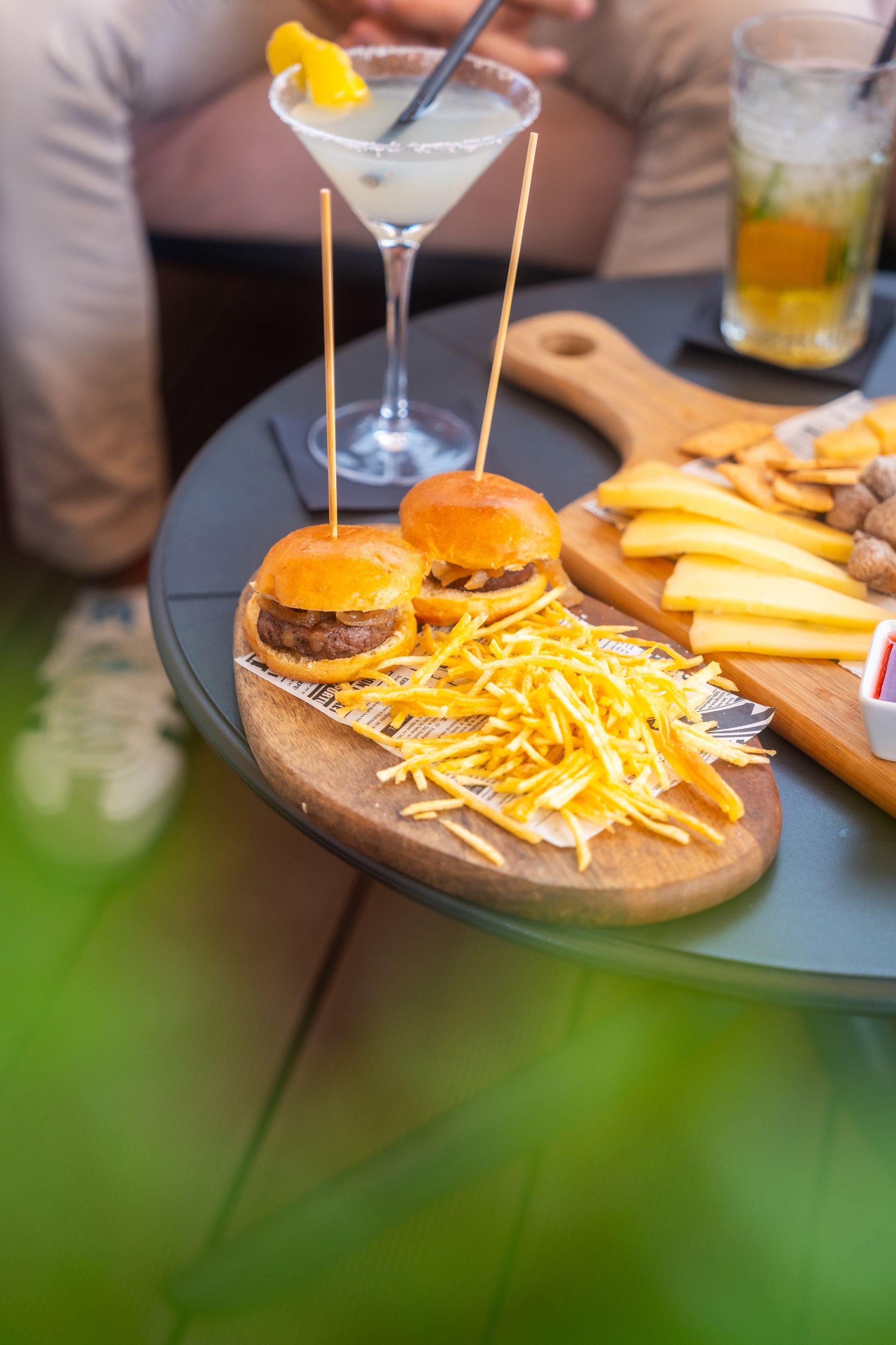 Cócteles y minihamburguesas sobre una mesa, con patatas fritas y una guarnición de martini cerca.