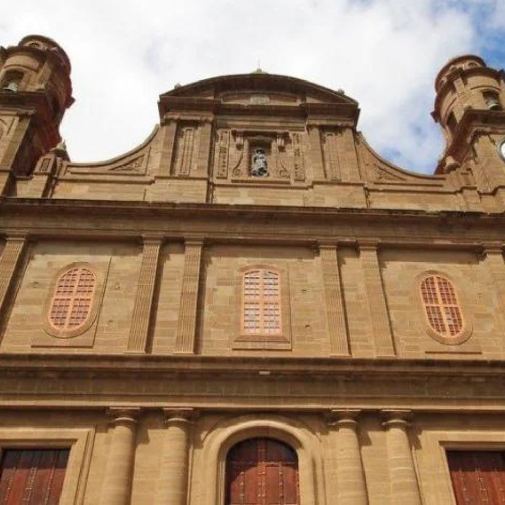 Fachada de una iglesia histórica de piedra con frontón central ornamentado y dos torres contra un cielo nublado.