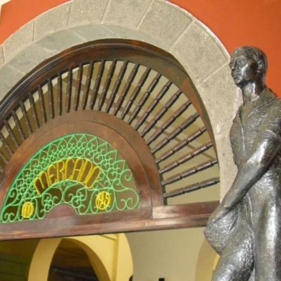 Figura de bronce junto a un ventanal decorativo arqueado con vidrieras verdes y doradas sobre una puerta.